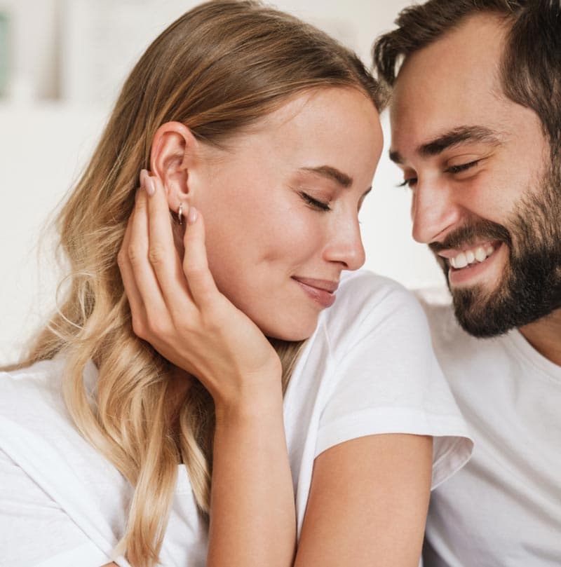 Man gently holding a woman's face as they smile at each other with affection.