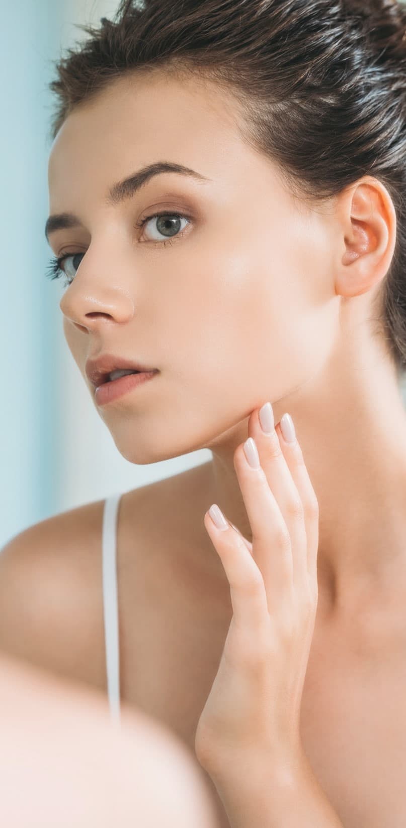 Young woman touching her face and looking at herself in the mirror