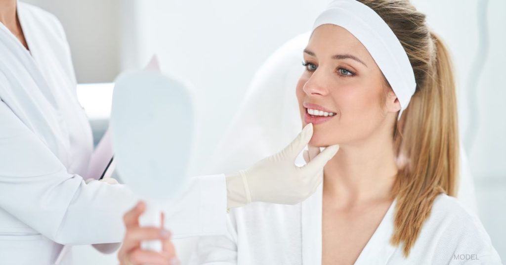 Young blonde woman examining her face in a handheld mirror at a doctor's appointment (models)