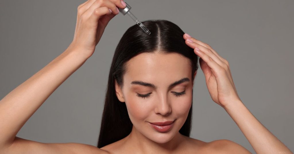 Woman is applying a liquid for hair loss treatment to her scalp. (MODEL)