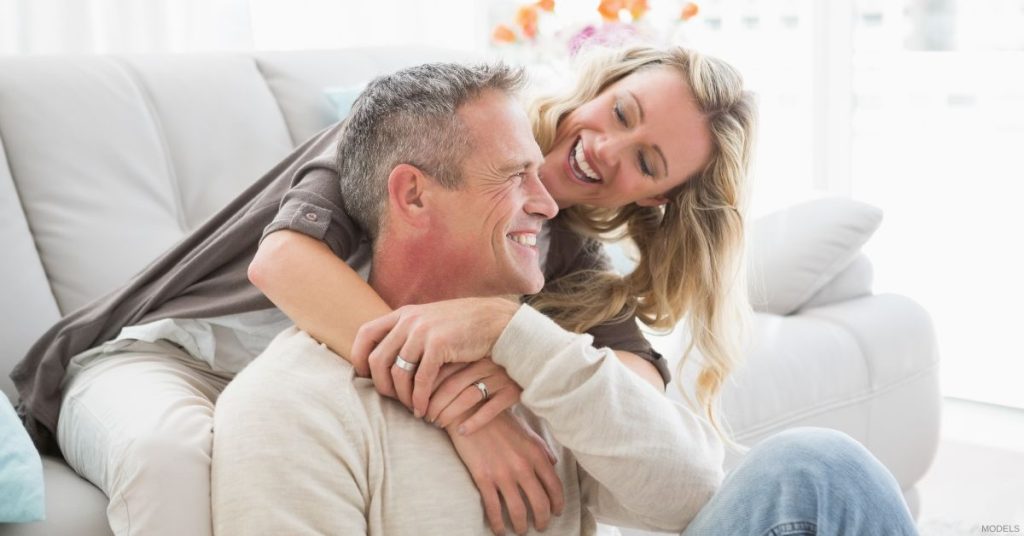 A mature happy couple hugging in front of a couch. (Models)